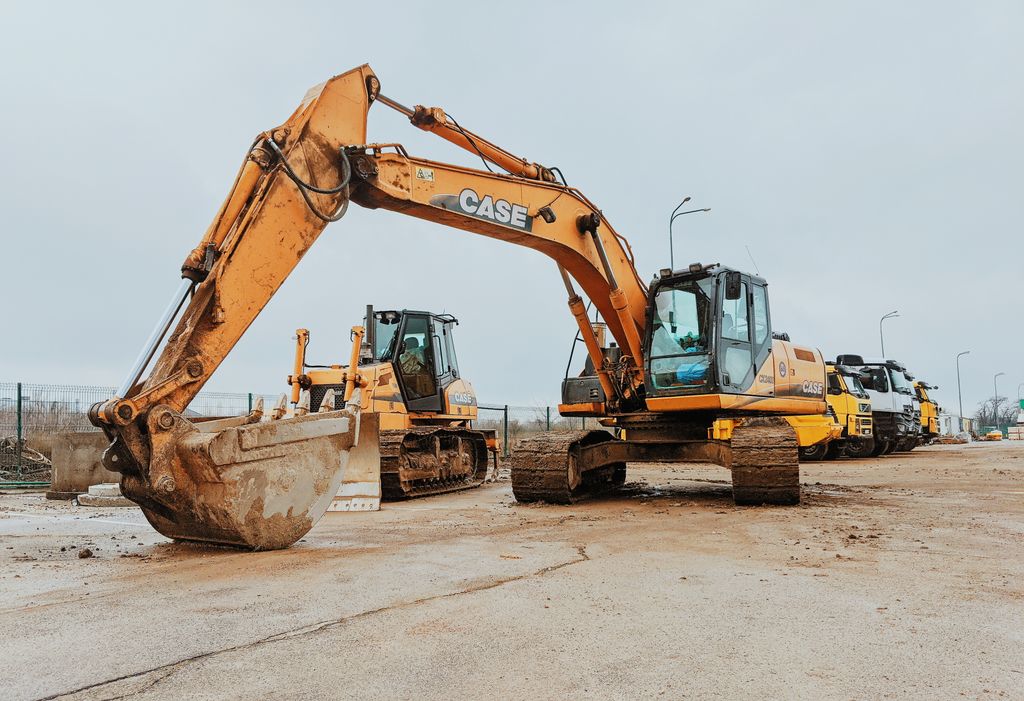 Big crawler excavator with bucket placed near stack of industrial machines in coastal terrain near sea against cloudless sky on street