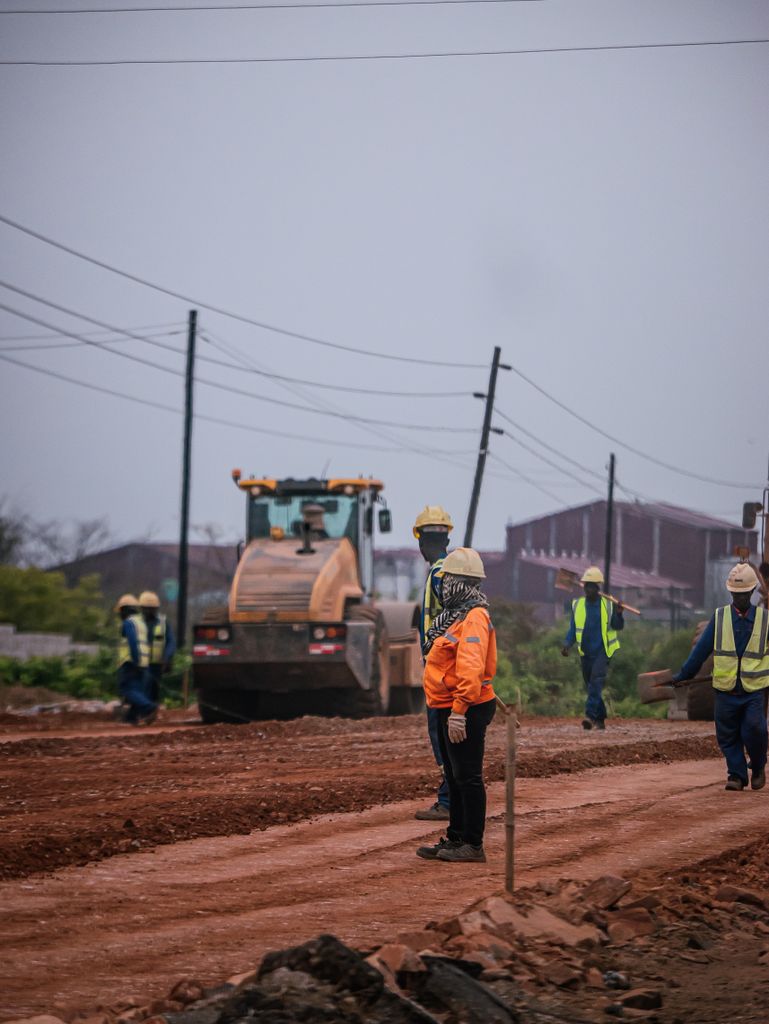 Construction workers at a road site operating heavy machinery, ensuring safety standards.